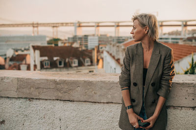 Young woman looking away while standing on railing in city