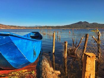 Boats moored in lake against clear blue sky