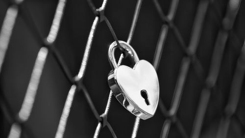 Close-up of heart shape padlock hanging on chainlink fence