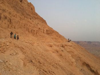 People walking on arid landscape against sky