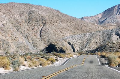 Road leading towards mountains against clear sky