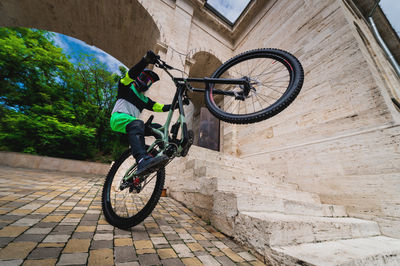 Man standing on one wheel of a mountain bike. horizontal shot outdoors in the city with architecture