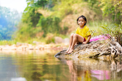 Portrait of cute girl sitting on rock by lake