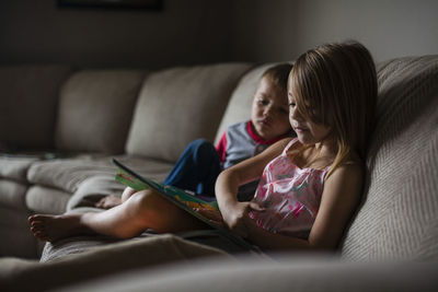 Siblings looking at picture book on sofa