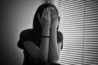 Woman covering face by window at home 