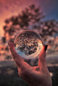 Close-up of hand holding crystal ball against sky