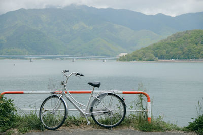 The bicycle is parked by the lake with the mountains in the background.