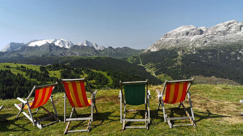 View of chairs on land against mountains and sky, dolomites