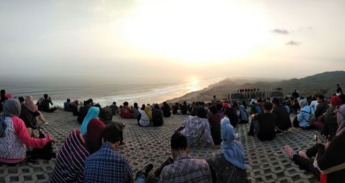 People looking at sea against sky during sunset