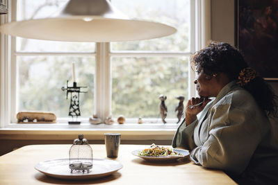 Contemplative mature woman having lunch on dining table at home