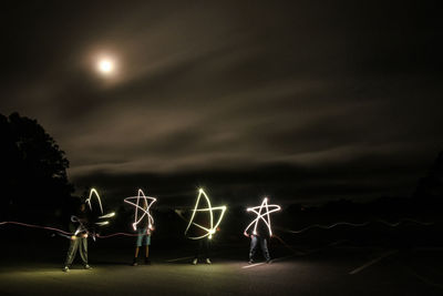 Family of stars. people on illuminated christmas lights against sky at night