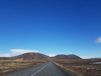 Road leading towards mountain against blue sky