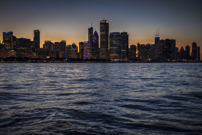 Sea by buildings against sky at dusk