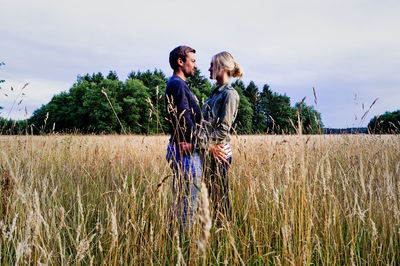 Happy couple standing on grassy field against sky