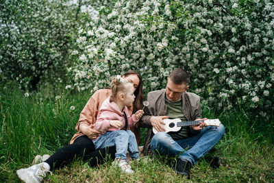 Family mom mom baby daughter in the garden blooming apple trees, father playing the ukulele