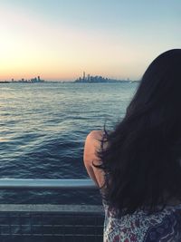 Rear view of woman by sea against sky during sunset