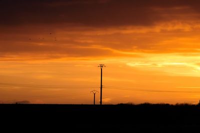 Silhouette electricity pylon against dramatic sky during sunset