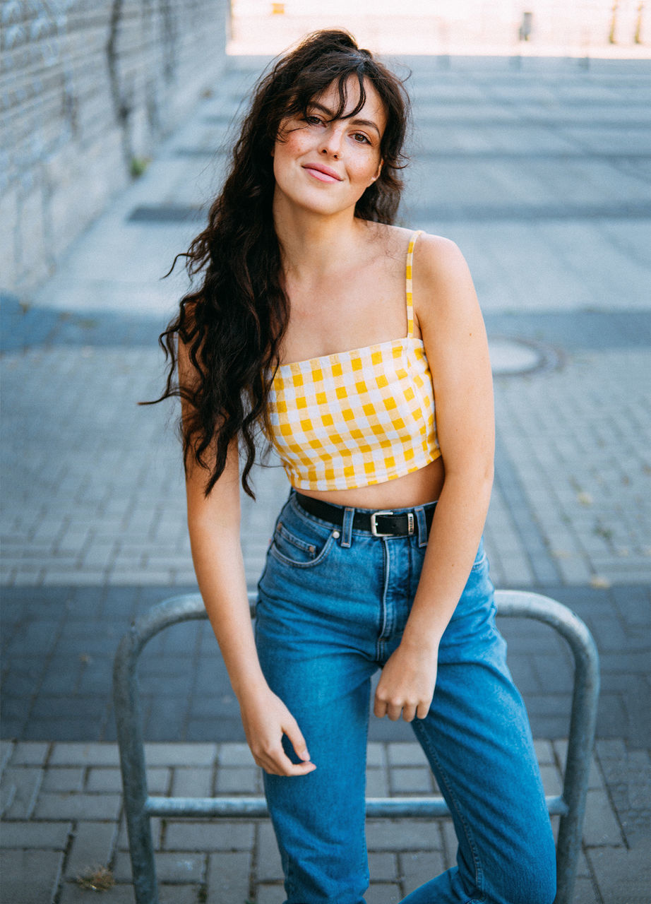 one person, casual clothing, three quarter length, front view, looking at camera, real people, portrait, focus on foreground, smiling, young adult, happiness, women, young women, leisure activity, standing, day, hair, lifestyles, architecture, beautiful woman, hairstyle, outdoors, jeans