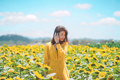 Woman standing on sunflower field against sky