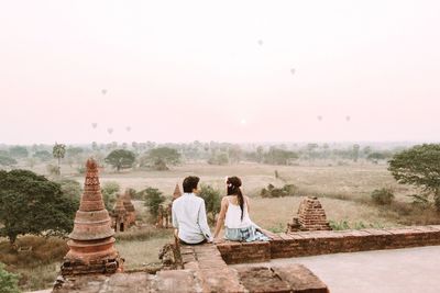 Rear view of friends sitting on temple against sky