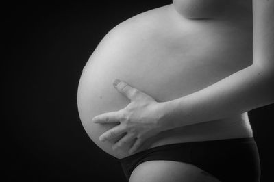 Midsection of pregnant woman touching stomach against black background