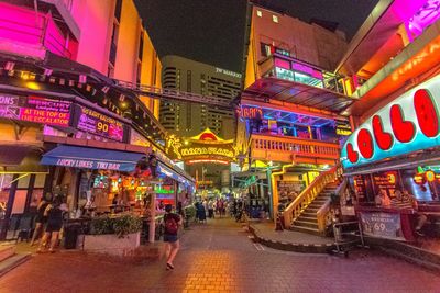 People on illuminated street amidst buildings in city at night