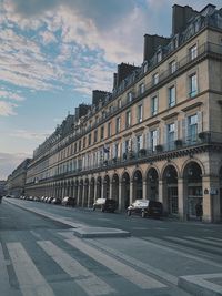 Cars on road by buildings against sky in city