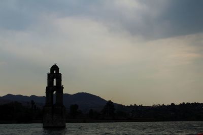 Lighthouse by sea against sky during sunset