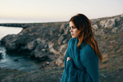 Young woman standing on rock by sea against sky