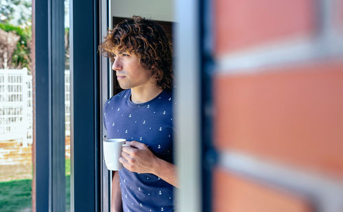 Man having coffee while standing at doorway