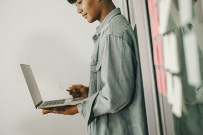 Side view of man using mobile phone against wall