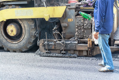 Low section of man standing by construction vehicle on road