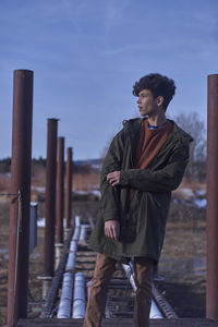 Young man standing by poles against sky