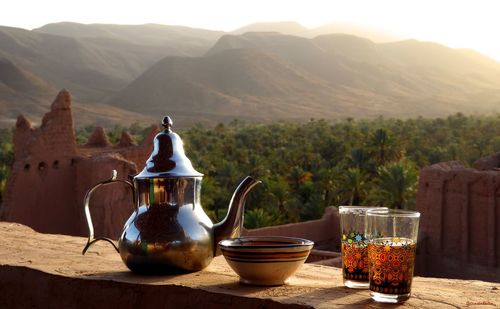 Metal teapot with drinking glasses on retaining wall against mountains