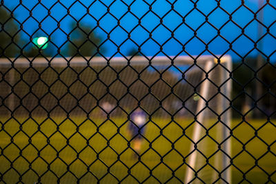 Goal post seen through chain-link fence at dusk