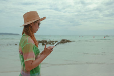 Woman using mobile phone at beach against sky
