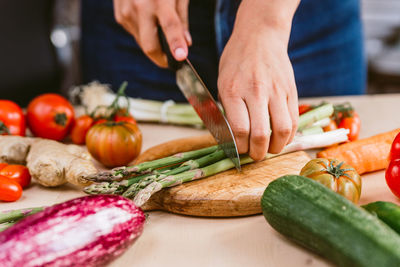 Preparing fresh asparagus meal on wood chopping board preparing in kitchen with fresh vegetables.