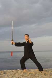 Man practicing tai chi at beach against cloudy sky