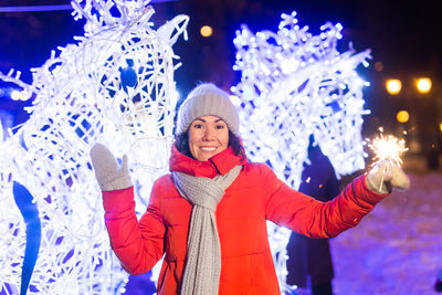 Portrait of smiling friends standing against illuminated christmas tree