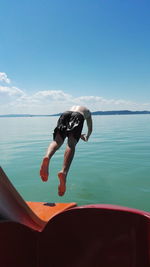 Man jumping in sea against blue sky