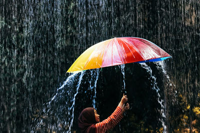 Side view of teenage girl holding umbrella in rain