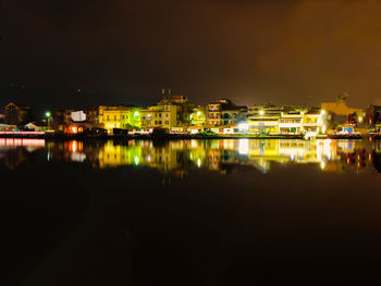 Illuminated buildings by lake against sky in city at night