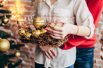 Midsection of couple holding container with christmas decorations at home