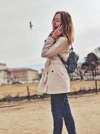 Side view of mid adult woman looking away while talking on mobile phone against sky