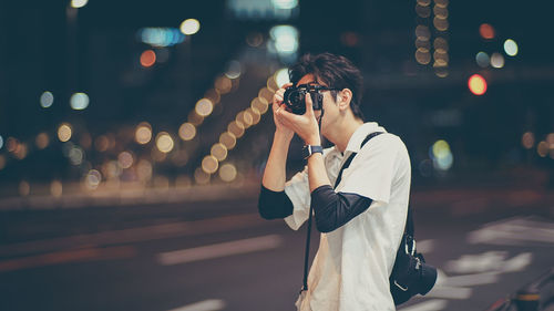 Young man photographing illuminated on street at night