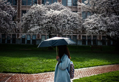 Woman with umbrella standing on grassy field against building during monsoon