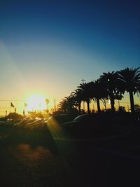 Silhouette palm trees by road against sky during sunset