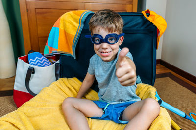 Portrait of boy gesturing while sitting in suitcase at home