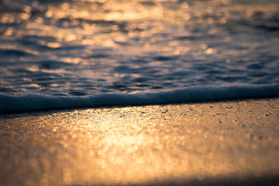 Close-up of surf on shore at beach during sunset