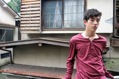 Teenage boy looking away while standing against window